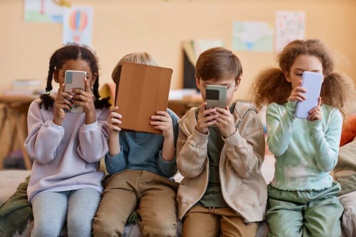 Four children sitting together, each engaged with their electronic devices