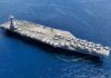 An aircraft carrier with numerous fighter jets on its deck in the ocean