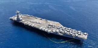 An aircraft carrier with numerous fighter jets on its deck in the ocean