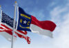 Flags of North Carolina and the United States waving against a blue sky