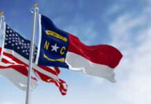 Flags of North Carolina and the United States waving against a blue sky