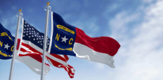Flags of North Carolina and the United States waving against a blue sky