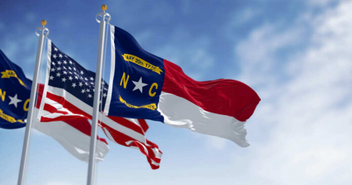 Flags of North Carolina and the United States waving against a blue sky