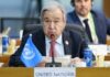 A man speaking at a United Nations conference with a blue UN flag in front of him
