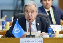 A man speaking at a United Nations conference with a blue UN flag in front of him
