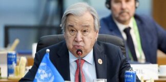 A man speaking at a United Nations conference with a blue UN flag in front of him