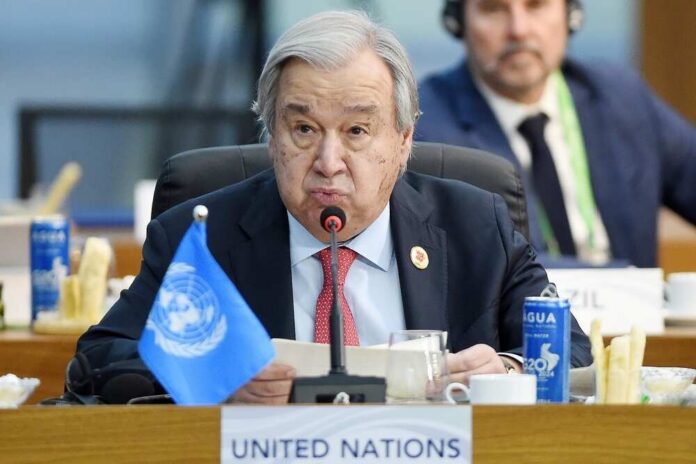 A man speaking at a United Nations conference with a blue UN flag in front of him