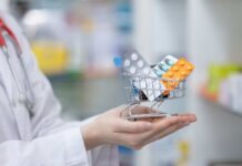 A doctor holding a miniature shopping cart filled with various medication packs