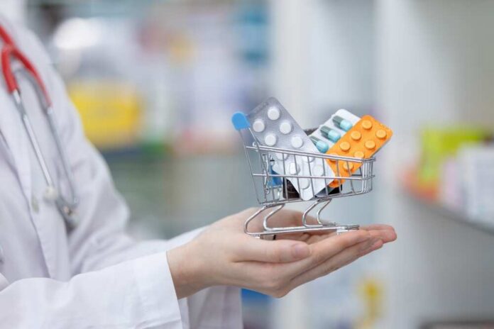 A doctor holding a miniature shopping cart filled with various medication packs