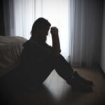 A silhouette of a woman sitting on the floor, appearing contemplative and distressed