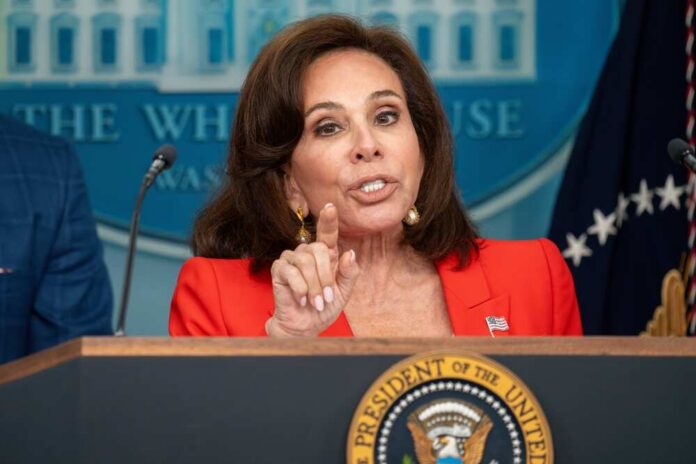A woman in a red blazer speaking at a podium with the Presidential seal