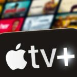 Close-up of a smartphone displaying the Apple TV+ logo with a blurred background of media thumbnails