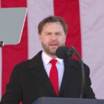 Man speaking at a podium with an American flag backdrop