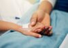 A patient holding hands with a loved one in a hospital setting