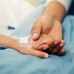 A patient holding hands with a loved one in a hospital setting