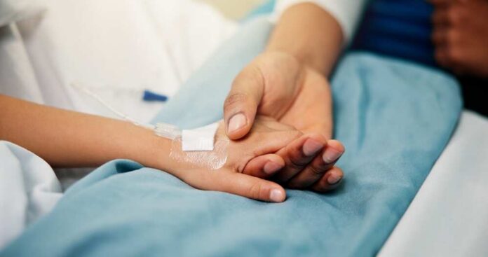 shutterstock_2704091397.jpg A patient holding hands with a loved one in a hospital setting