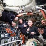 Four astronauts in a spacecraft, smiling and giving thumbs up