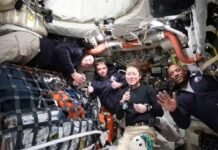 Four astronauts in a spacecraft, smiling and giving thumbs up
