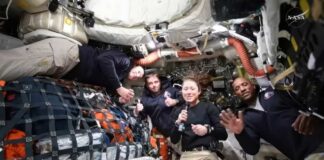 Four astronauts in a spacecraft, smiling and giving thumbs up