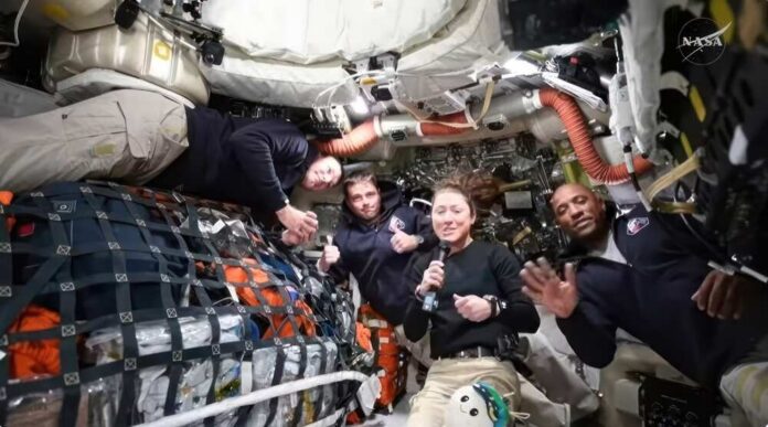 Four astronauts in a spacecraft, smiling and giving thumbs up