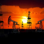 Silhouetted oil rigs against a vibrant sunset