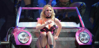 A performer in a pink outfit sitting on a colorful car during a concert