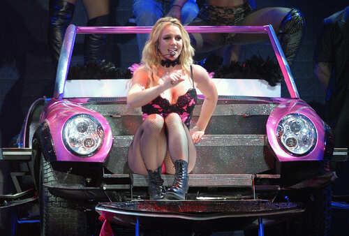 shutterstock_761995468.jpg A performer in a pink outfit sitting on a colorful car during a concert