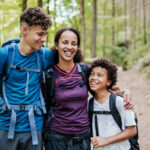 A mother and her two children smiling while hiking on a forest trail
