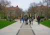 Students walking along a pathway on a university campus with historic buildings in the background