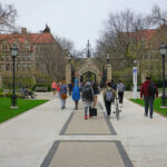 Students walking along a pathway on a university campus with historic buildings in the background