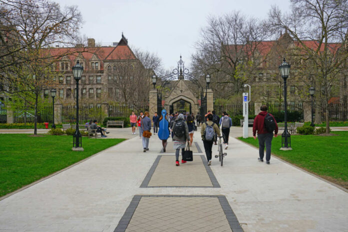 Students walking along a pathway on a university campus with historic buildings in the background