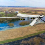 A military drone flying over a rural landscape with a river
