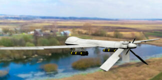 A military drone flying over a rural landscape with a river