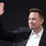 A man in a suit waving with a smile during a conference