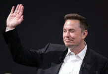 A man in a suit waving with a smile during a conference