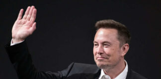 A man in a suit waving with a smile during a conference