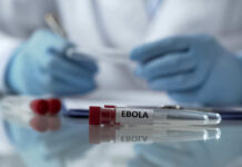 Ebola test tube on lab table with gloved researcher in background