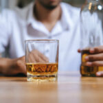 A man holding a whiskey glass and a bottle in a bar setting