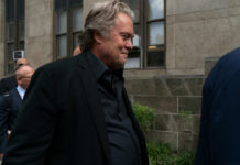 Bannon’s War Room Shakes Media — Unstoppable! A man in a black jacket walking past a group of people outside a building
