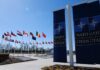 U.S. Threatens NATO Allies? The Inside Story Flags of various nations displayed outside NATO headquarters under a clear blue sky