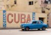 Frightening Cuba Encounter: Is Reporting a Crime? A vintage blue car driving past a large mural that says 'Viva Cuba'
