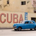 Frightening Cuba Encounter: Is Reporting a Crime? A vintage blue car driving past a large mural that says 'Viva Cuba'