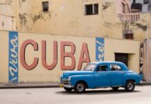 Frightening Cuba Encounter: Is Reporting a Crime? A vintage blue car driving past a large mural that says 'Viva Cuba'