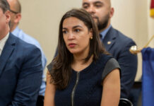 AOC’s Tennessee Claim Falls Apart—Here’s Why A woman in a dark dress sitting among a group, appearing engaged in discussion