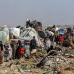 Displaced families with belongings crowd a rubble-strewn road