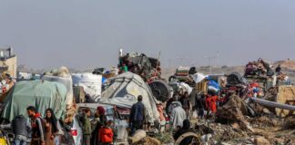 Displaced families with belongings crowd a rubble-strewn road