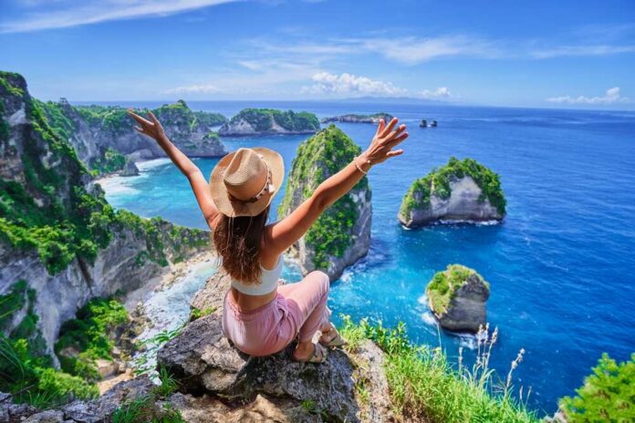 Woman sitting on a cliff with arms raised, overlooking a beautiful ocean view