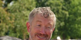 A smiling man in a suit engaging in conversation outdoors