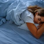 A woman sleeping peacefully on a bed with blue sheets