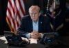 4% Drop: Trump Name Hurts Republicans? A serious-looking man seated at a table with phones and an American flag in the background
